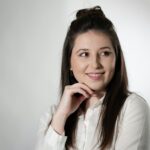 Professional portrait of a smiling woman in a white shirt, exuding confidence and friendliness.